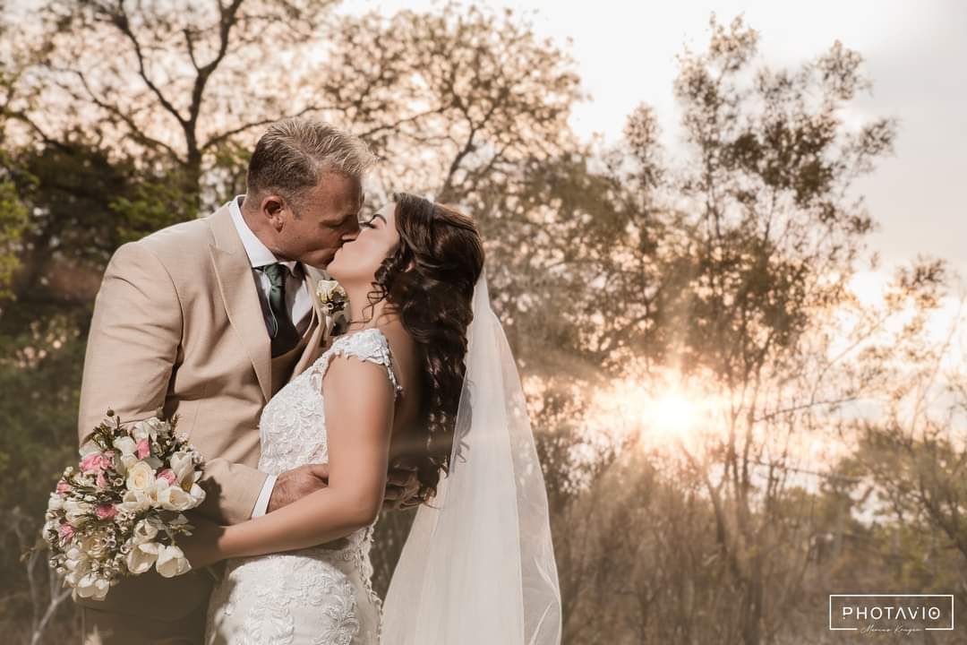 A bride and groom are kissing in a field with trees in the background at Riverside Castle.