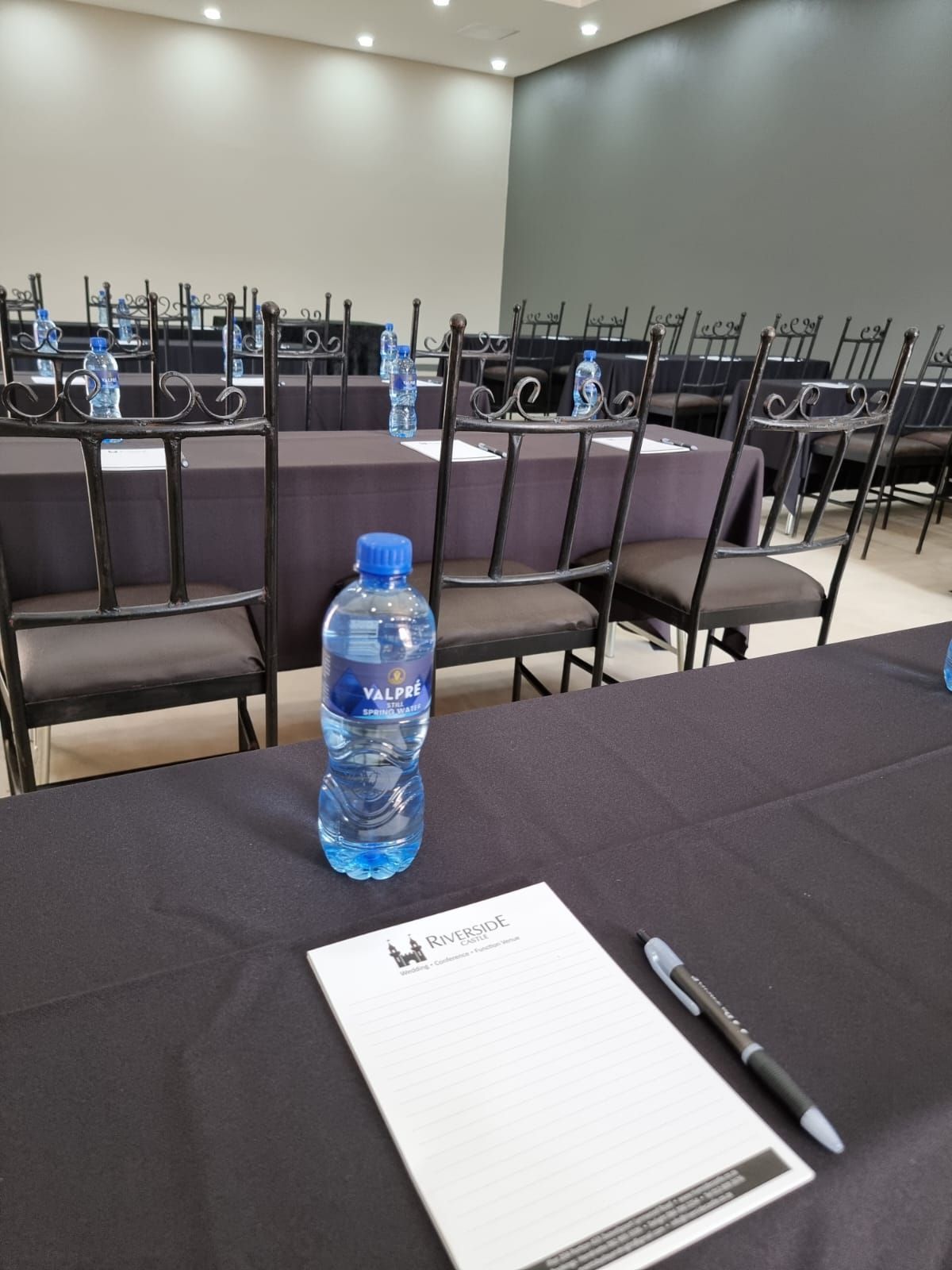Conference room with rows of chairs, a blue water bottle, and a notepad with a pen on a table.