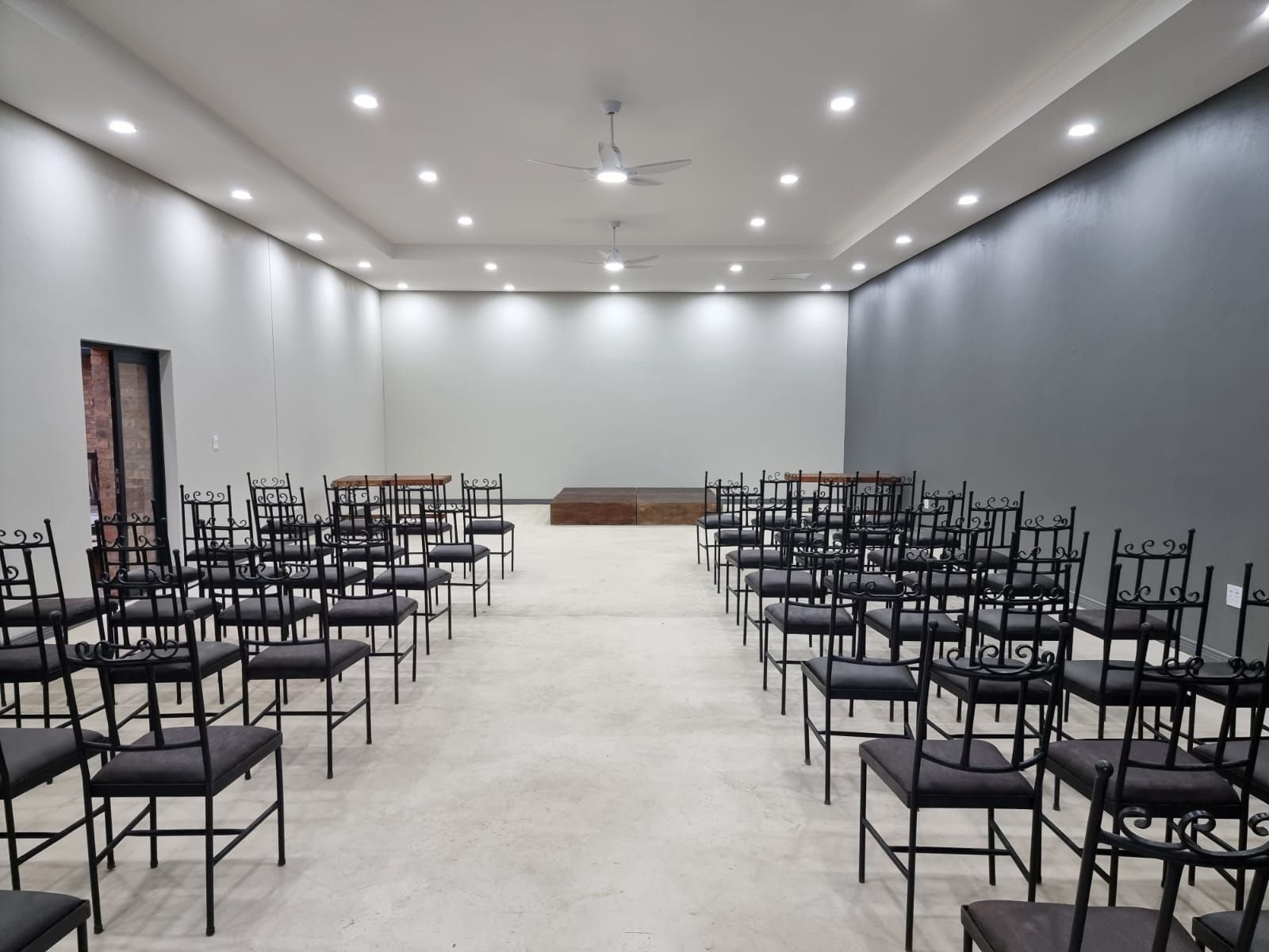 Empty conference room with rows of black chairs facing a small stage under recessed ceiling lights