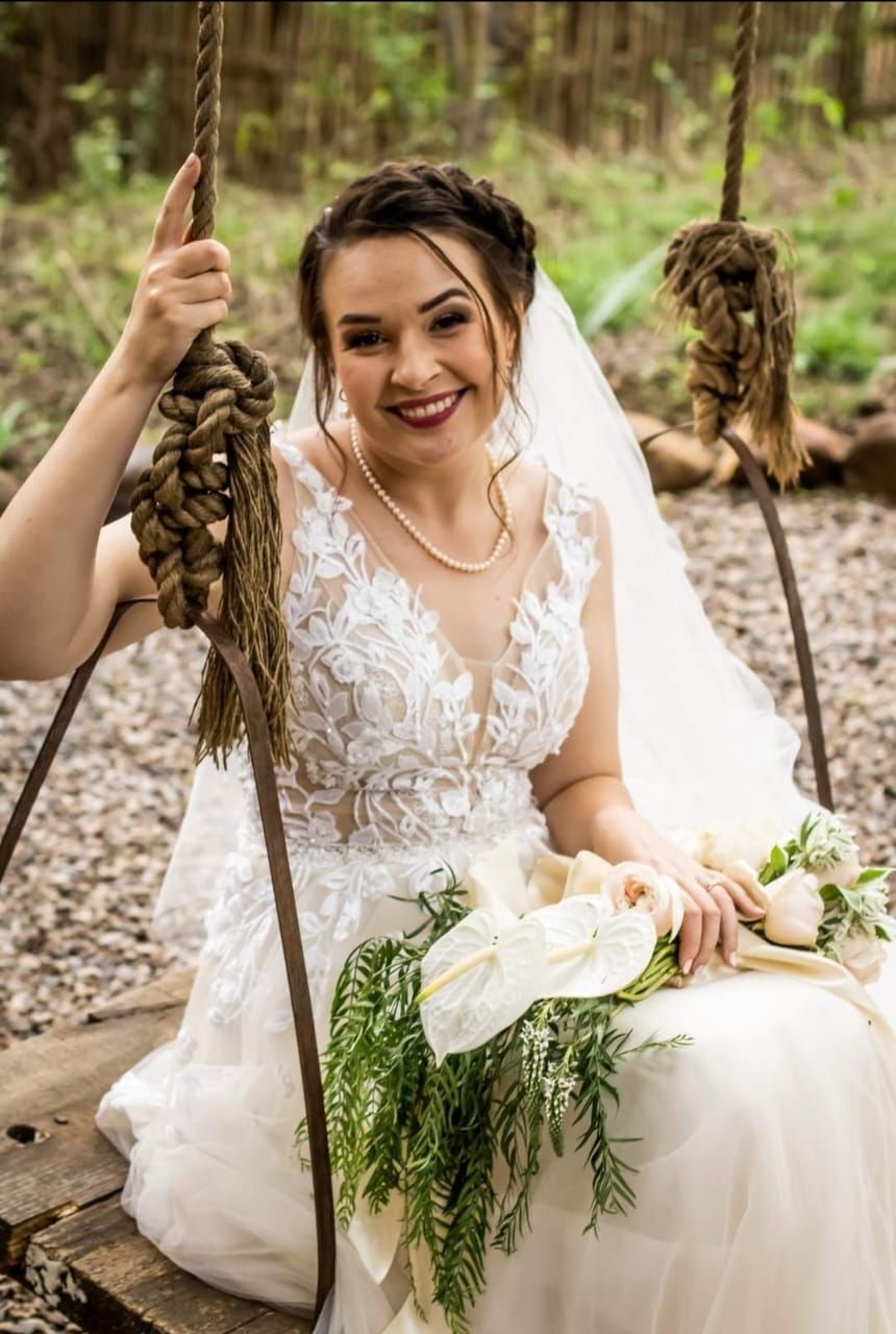 A bride in a wedding dress is sitting on a swing near Fairywoods at Riverside Castle.