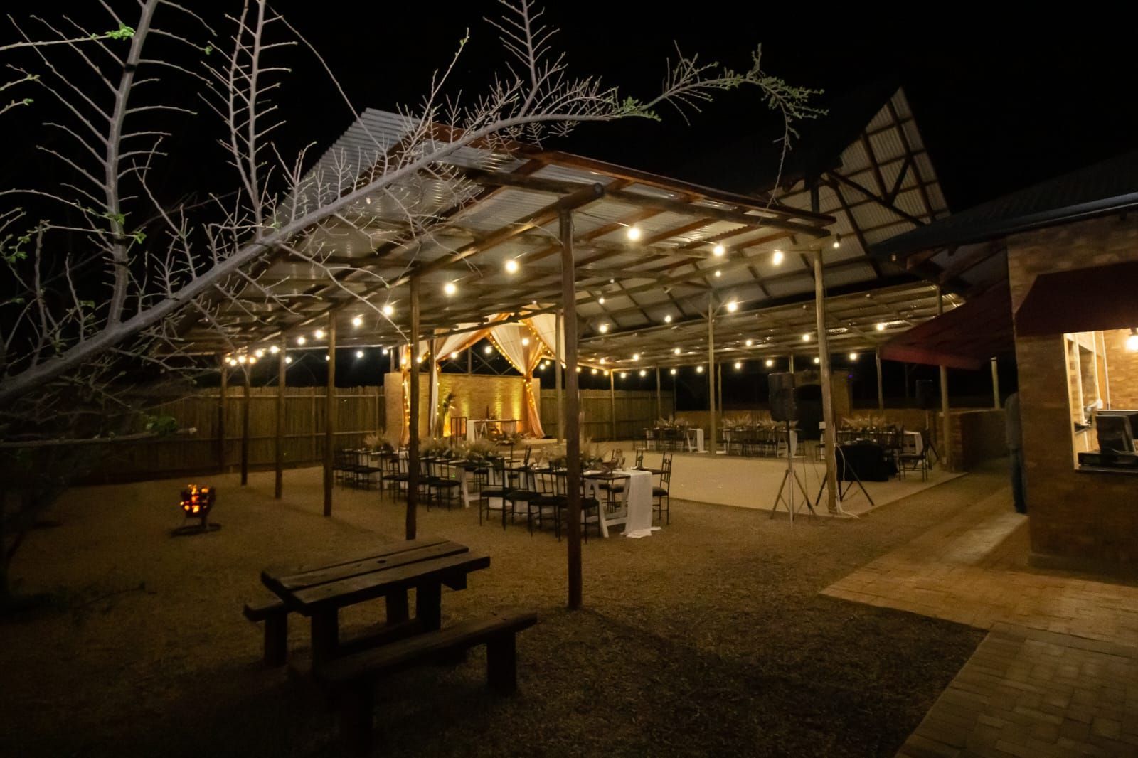 Outdoor dining area at night with string lights, picnic tables, and a covered pavilion