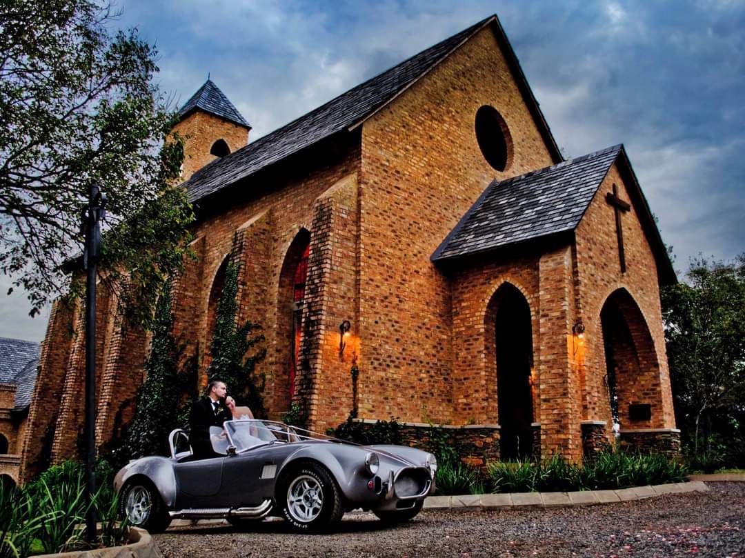 A couple is sitting in a sports car in front of the Riverside Castle Chapel.