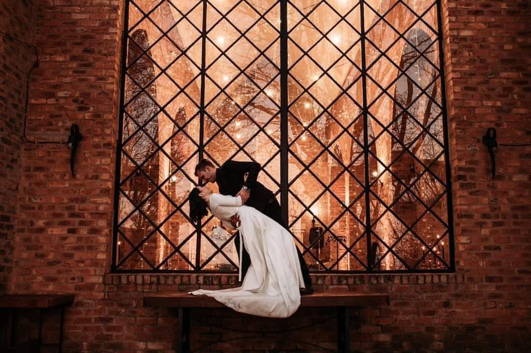 A bride and groom are kissing in front of a large window.