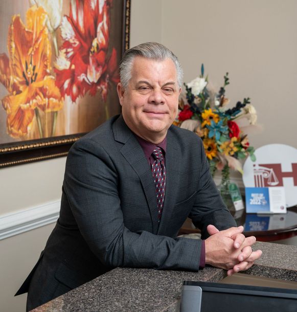 Man in a suit smiles, leaning on a counter near a flower arrangement and painting.