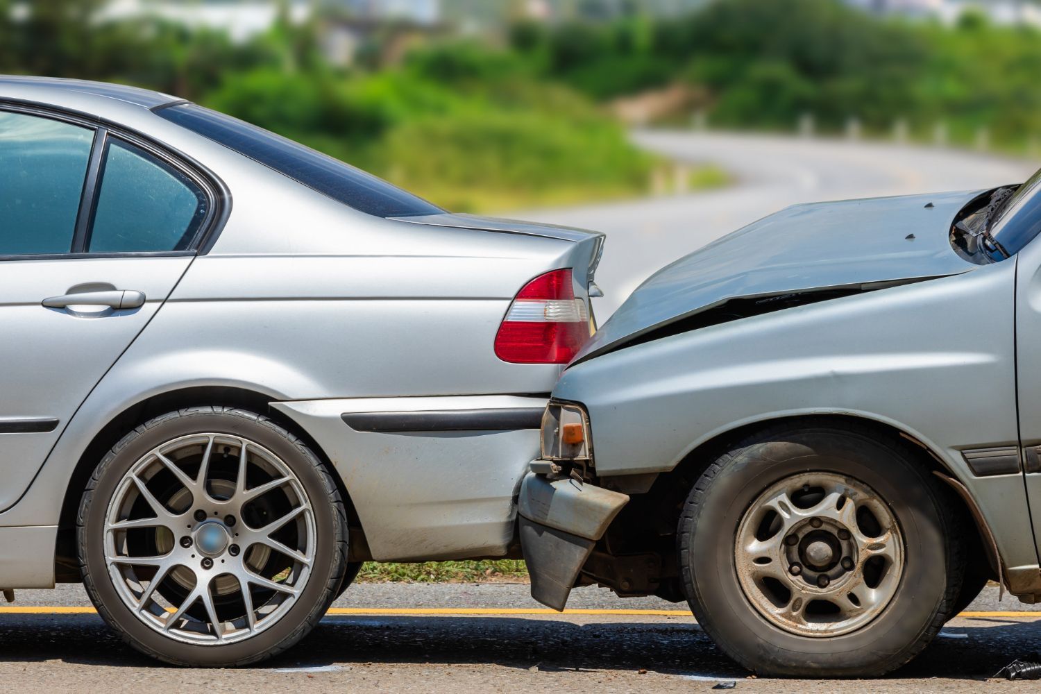 Damaged black car involved in a traffic accident, debris on the road, other cars in the background.
