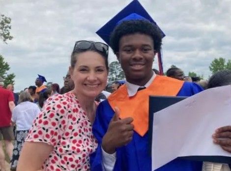 Woman and graduate in blue cap and gown smiling with thumbs up, holding diploma.