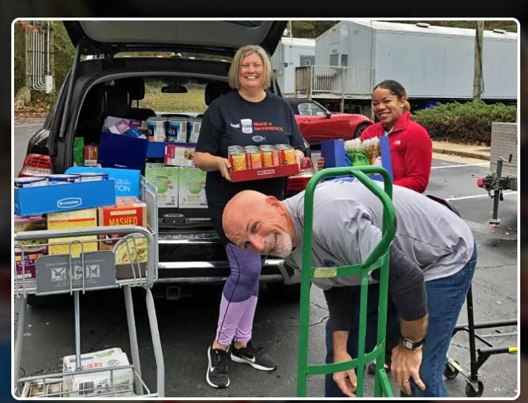 Volunteers unloading donations from a car trunk. Canned goods and boxes being moved with a cart.