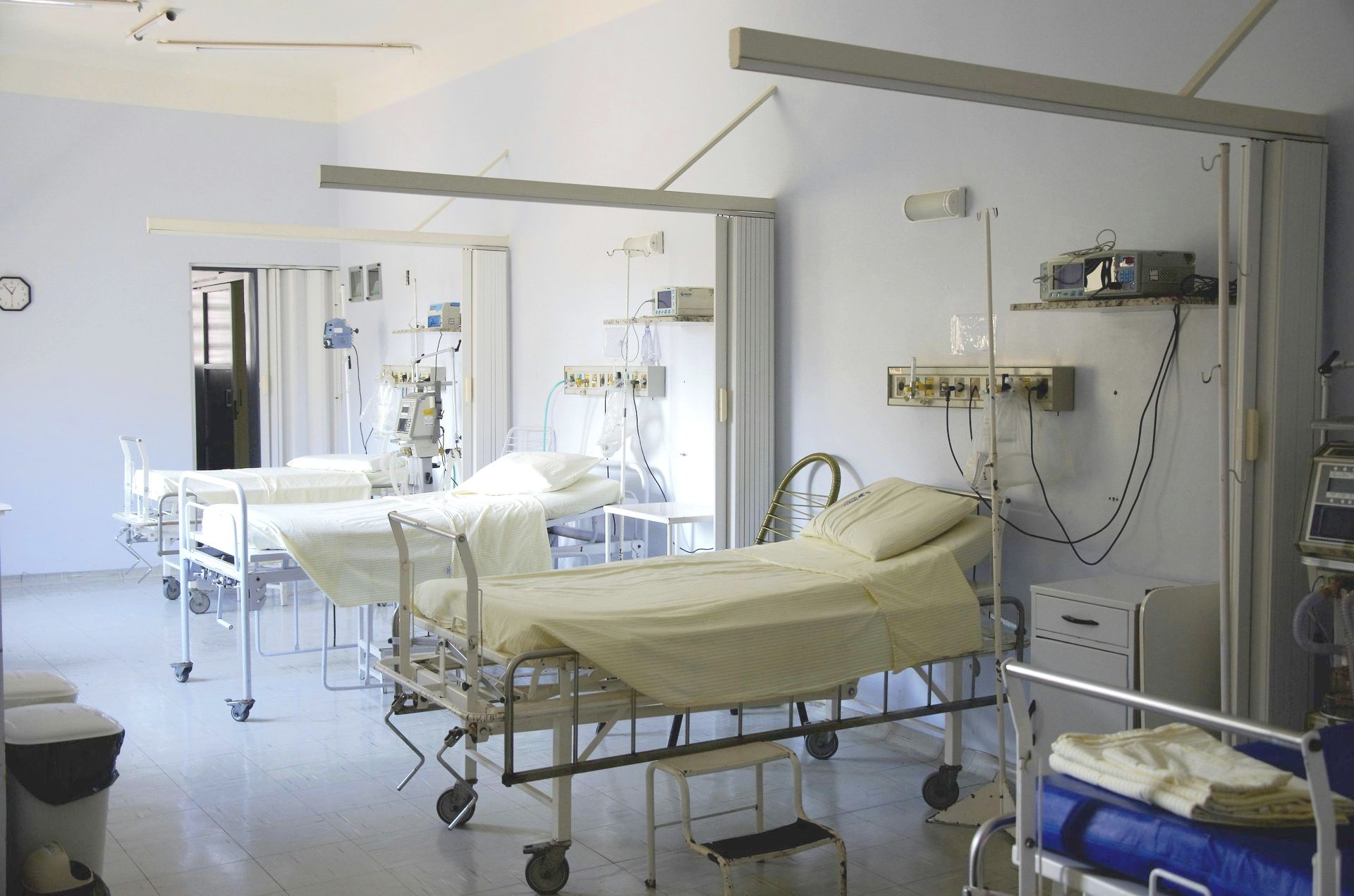 Hospital room with three empty beds, medical equipment, and white walls.