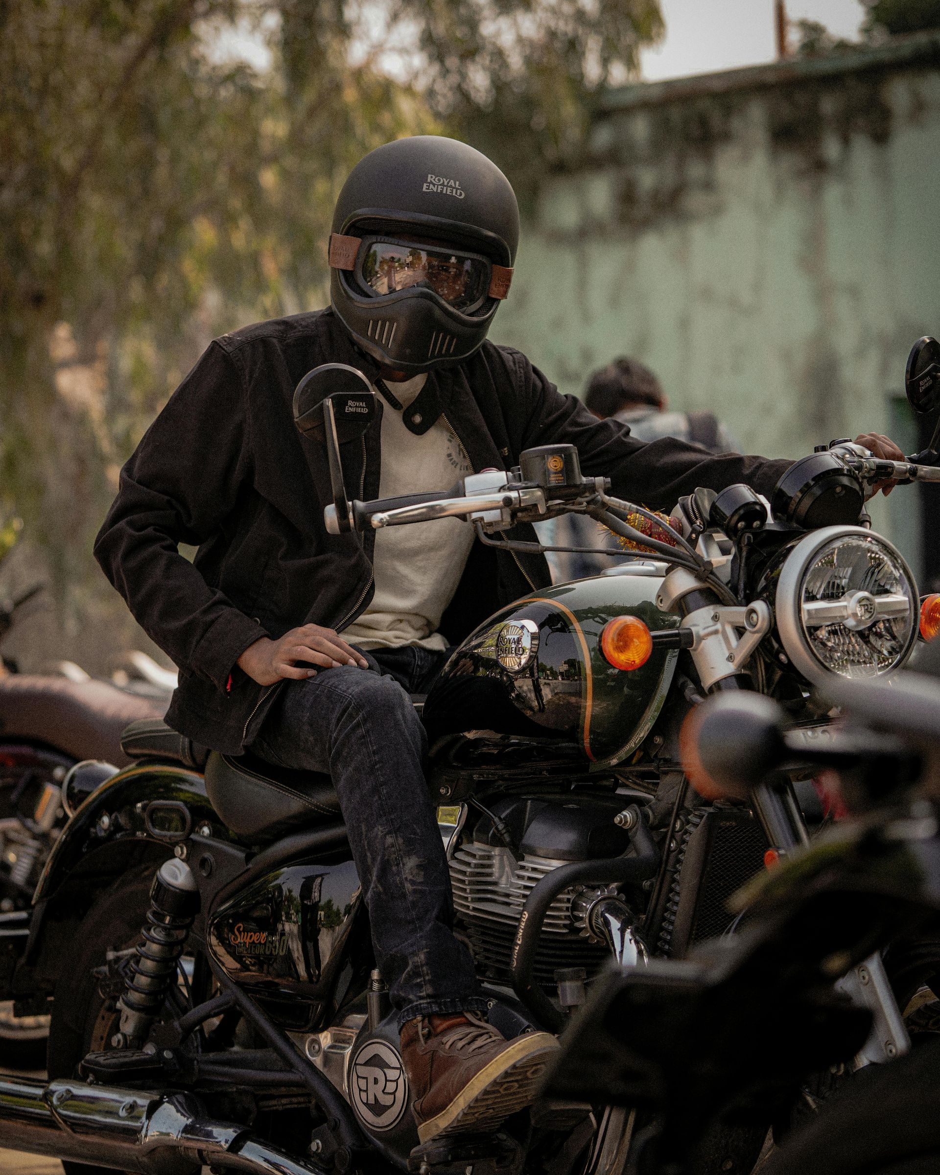 Person wearing a helmet sits on a motorcycle, outdoor setting, possibly a gathering.