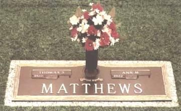 Grave marker with pink and white flowers and the name Matthews engraved on a bronze plaque.