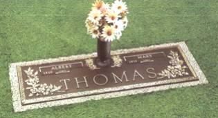 Grave marker with flowers on a green lawn, engraved with the name Thomas