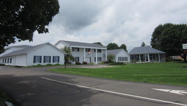 White building with blue shutters beside a road, on a grassy lawn under cloudy skies.