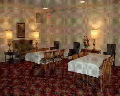 Quiet dining room with white-clothed tables, wooden chairs, wall lamps, and patterned carpet