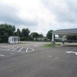 Empty parking lot beside a covered pavilion and small white building under cloudy skies