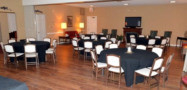 Empty event room with round tables, white chairs, wood floor, and a podium at the front