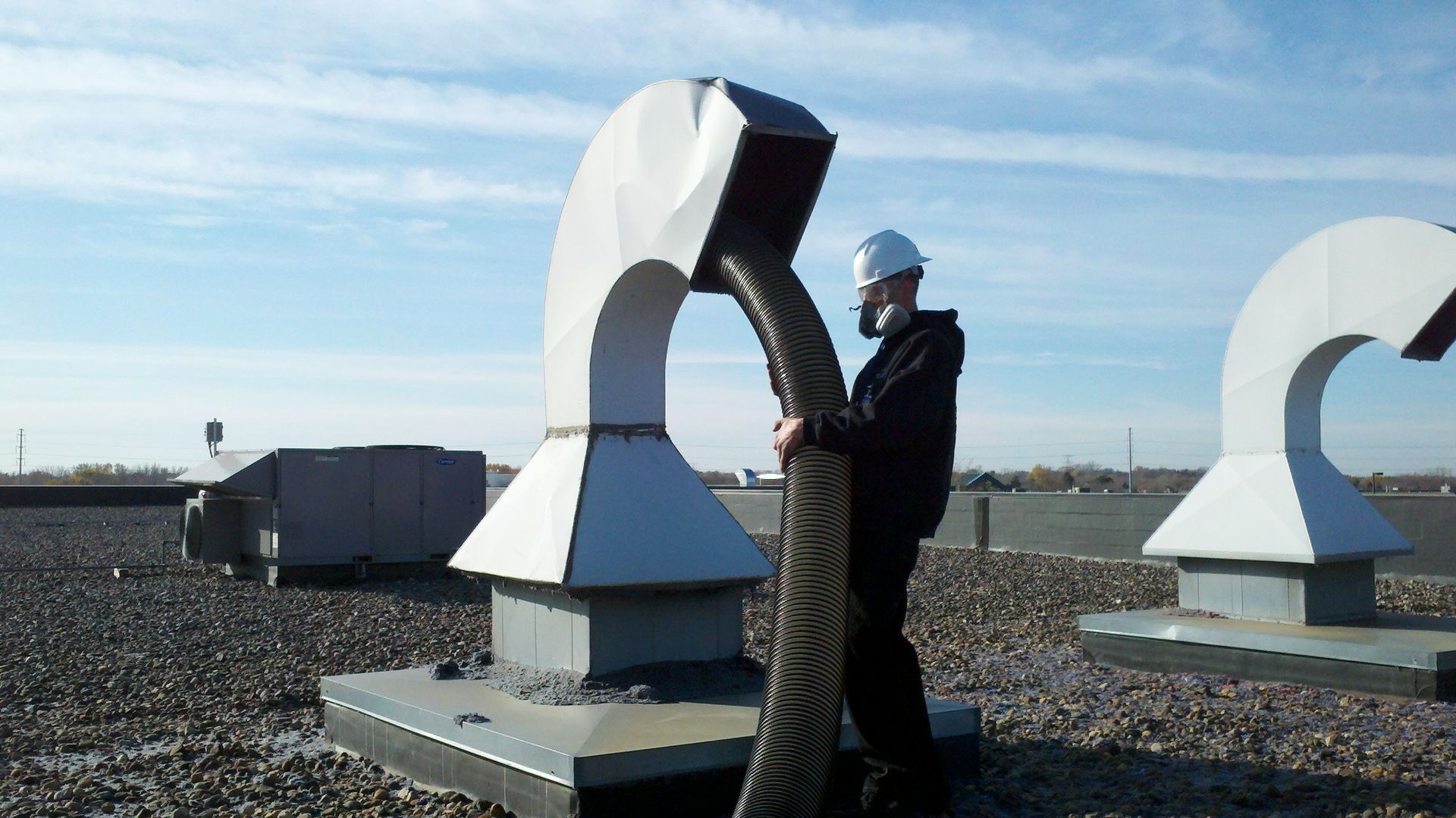 Man in hard hat working on rooftop ventilation system.