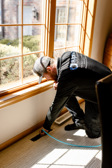Person cleans HVAC vent with a rotating brush tool.