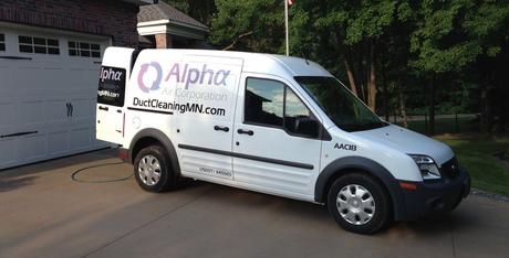 White Alpha van parked on a driveway in front of a garage. The van has branding on its side.