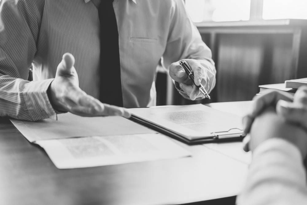 Man in a Suit Gestures With His Hands, Explaining Document to Another Person — Paradise Law In Beaudesert, QLD