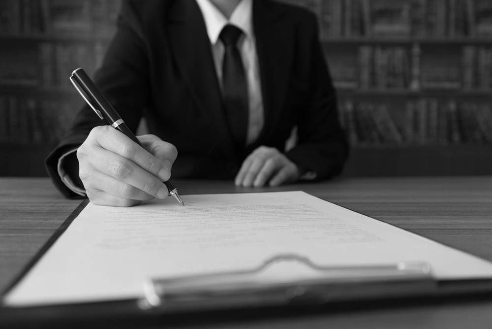 Person in a Suit Signing a Document on a Clipboard With a Pen at a Desk — Paradise Law In Coolangatta, QLD
