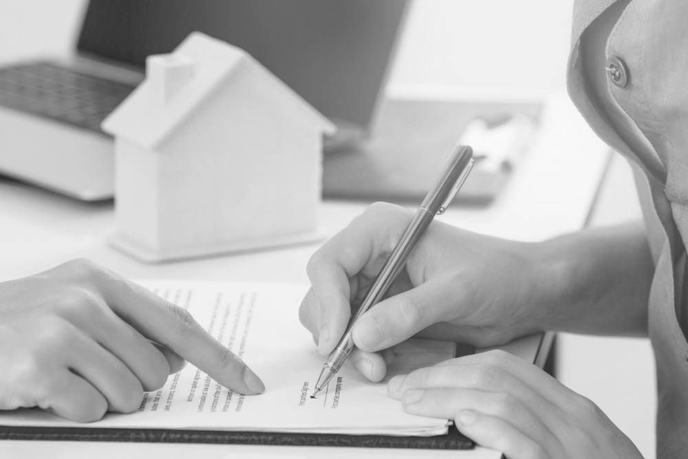 Person Signing a Document, Another Person Pointing. A Model House and Laptop Sit Nearby — Paradise Law In Coolangatta, QLD