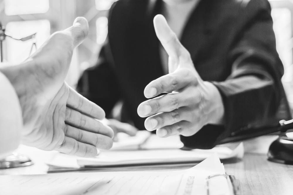 Two People Reaching Out to Shake Hands at a Desk With Documents — Paradise Law In Surfers Paradise, QLD