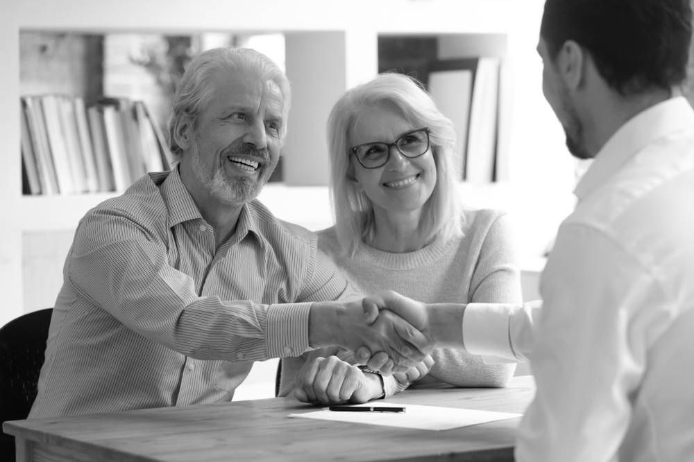 Older Couple Shaking Hands With a Person, Sitting at a Table With Documents — Paradise Law In Caloundra, QLD