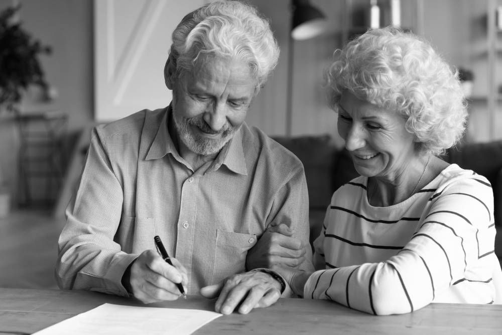 Older Person Signing Document; Another Person Looks on Smiling — Paradise Law In Tweed Heads, NSW
