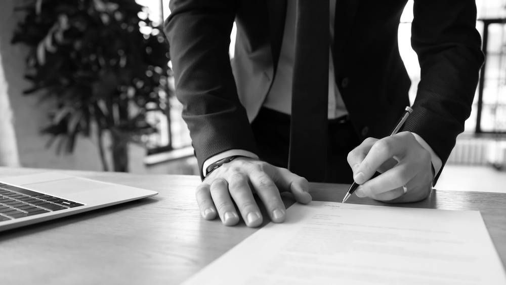 Person in Suit Signing Document at a Desk With a Laptop — Paradise Law In Noosa, QLD