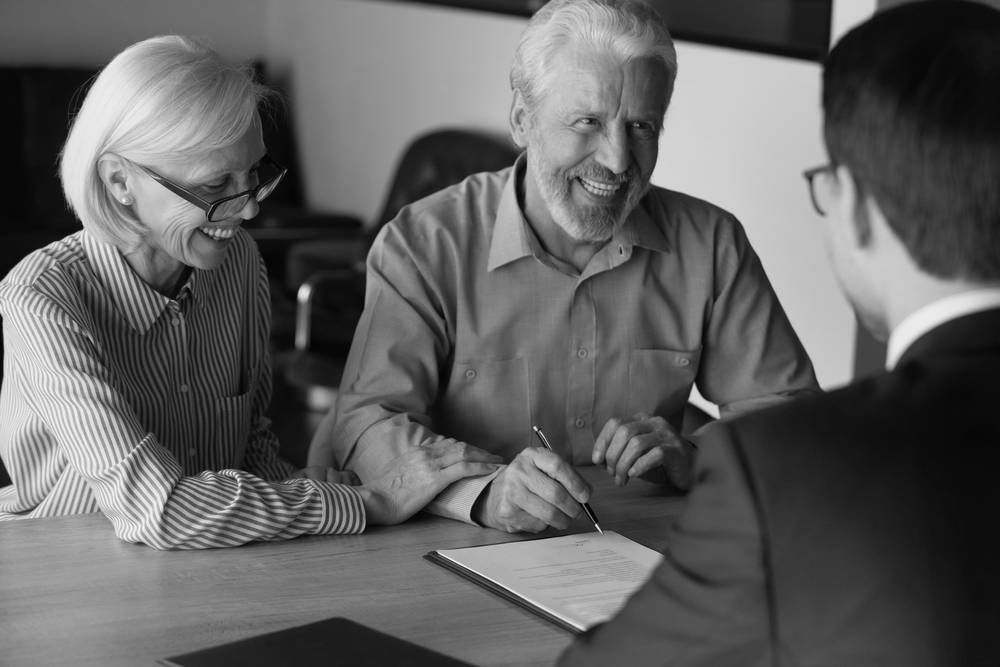 Older Couple Smiling While Reviewing Paperwork With a Professional at a Table — Paradise Law In Surfers Paradise, QLD