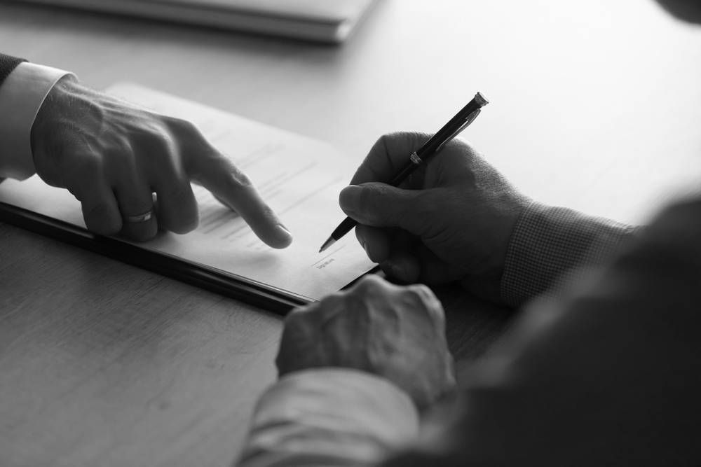 Person Signing a Document, Another Pointing at a Specific Line on the Page — Paradise Law In Surfers Paradise, QLD