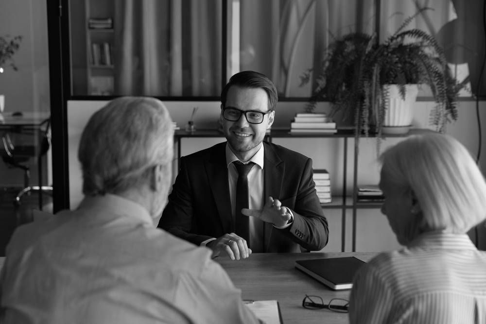 Man in Suit Gestures, Speaking to a Seated Older Couple at a Desk — Paradise Law In Caloundra, QLD