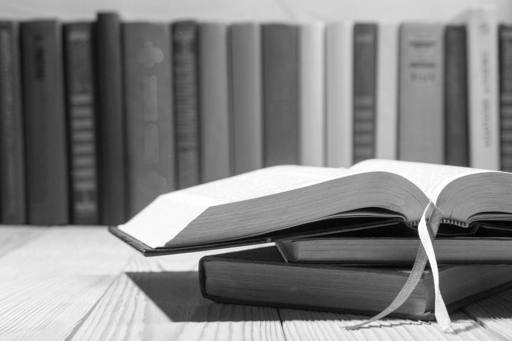 Books Stacked on a Wooden Surface, One Open With a Red Ribbon, Others on a Shelf in the Background — Paradise Law In Surfers Paradise, QLD