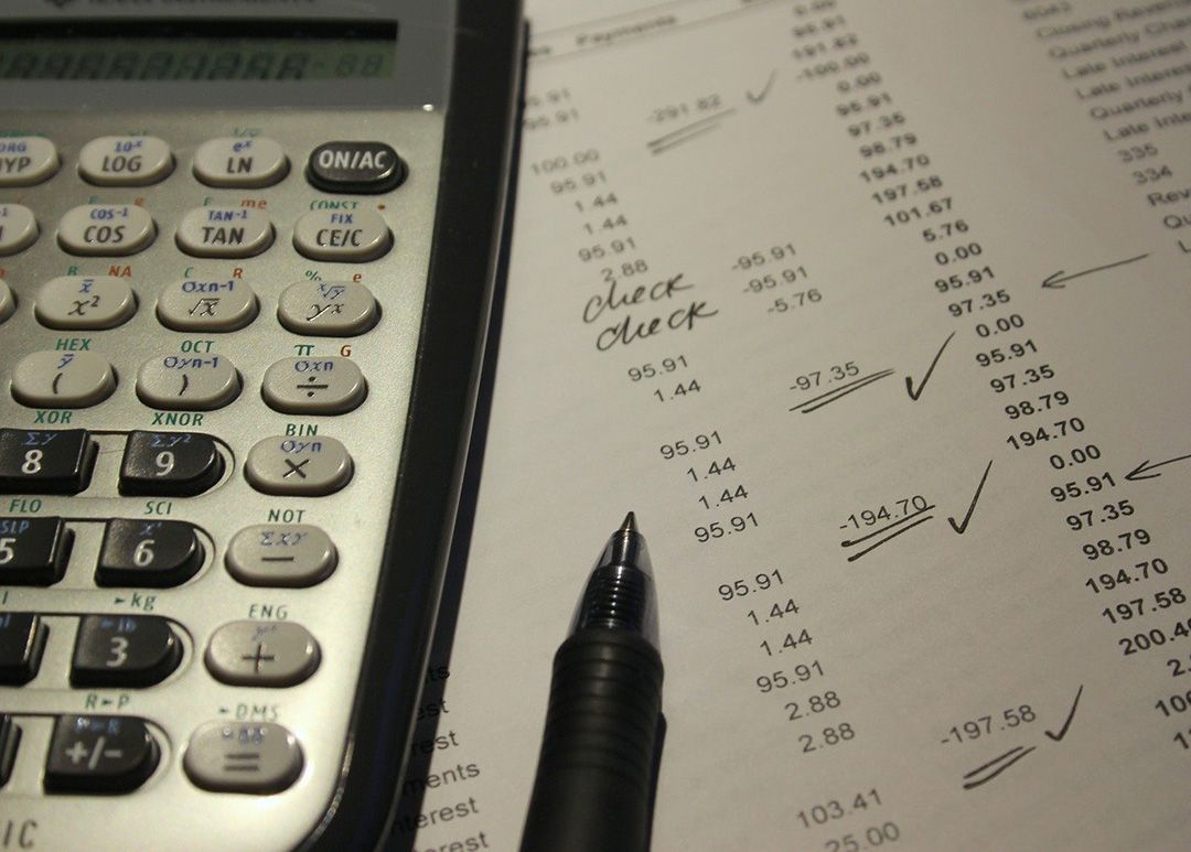 Calculator, pen, and financial document with handwritten notes and check marks.