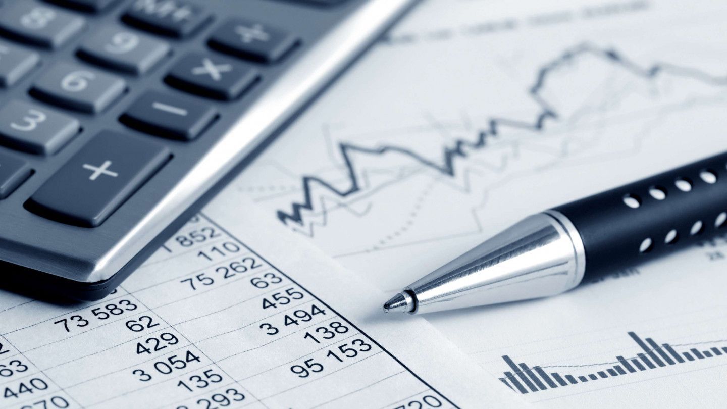 Calculator, pen, and financial charts on paper, likely for analysis or accounting purposes.