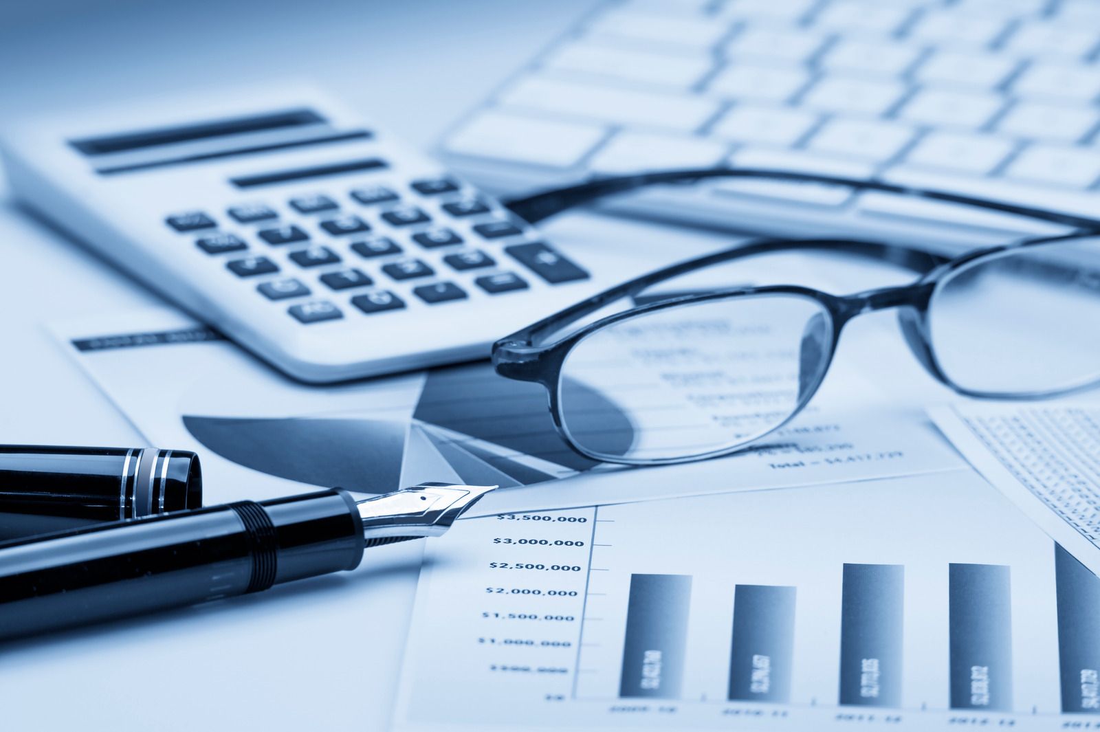 Calculator, glasses, pen, keyboard, and bar graph on financial documents.