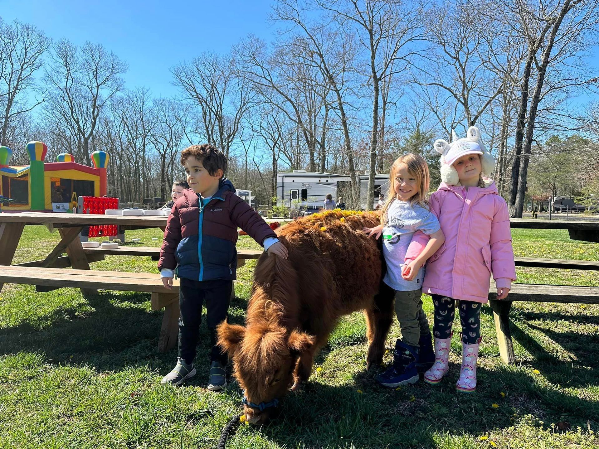 Three children stand with a small pony grazing in a sunny park.