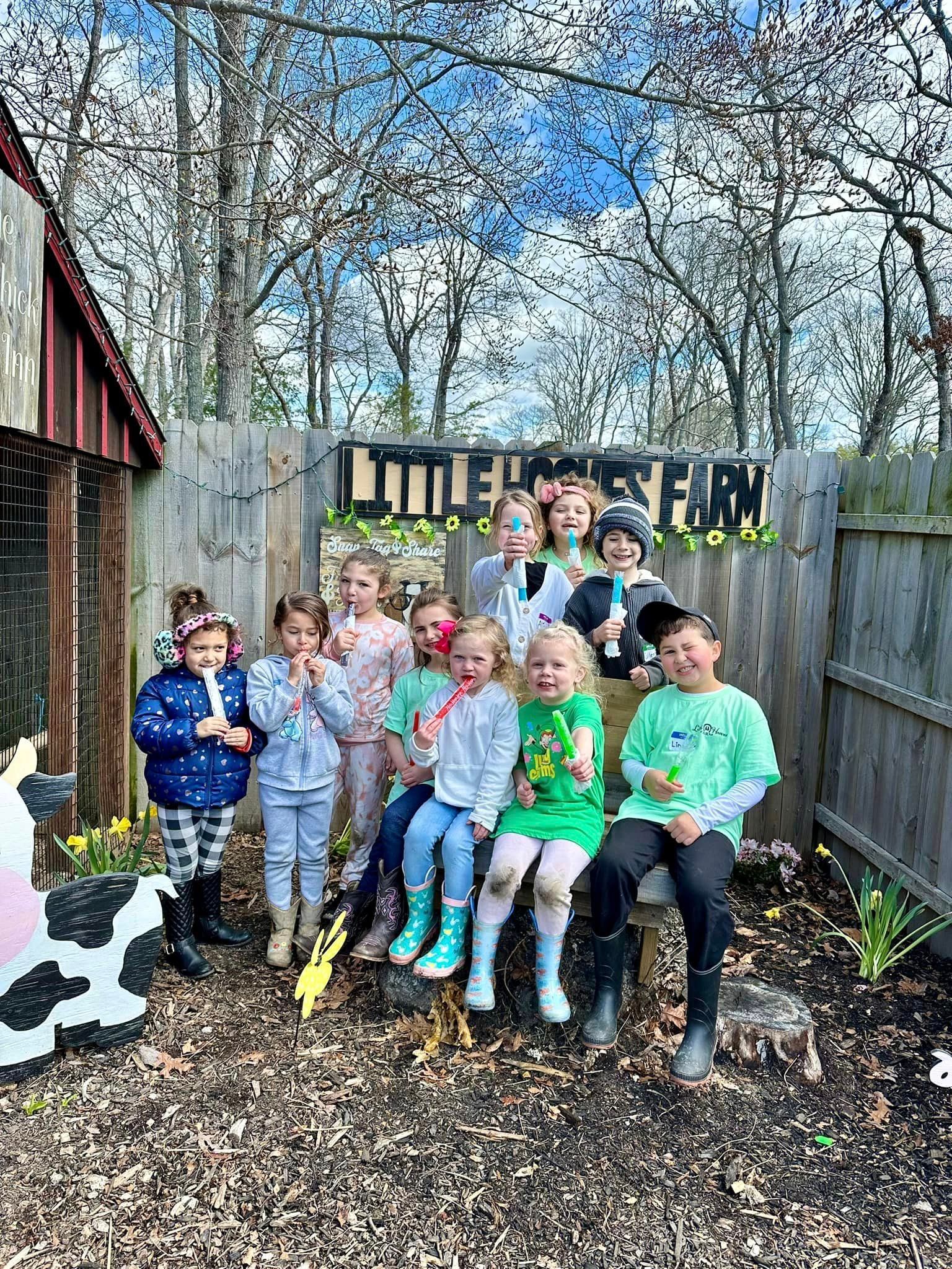 Children sitting on a bench in a leafy backyard, smiling and holding flowers in front of a fence