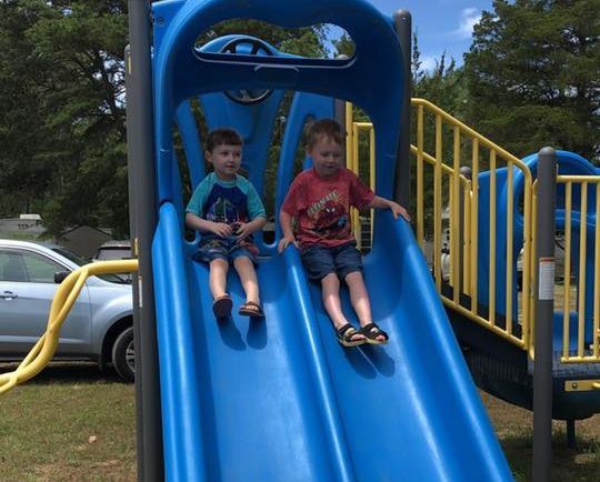 Two young boys are sliding down a blue slide at a playground.