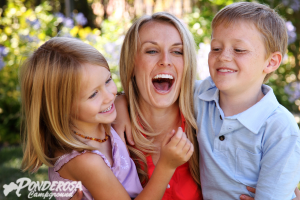 Smiling woman in red shirt laughing with two children outdoors in a sunny garden