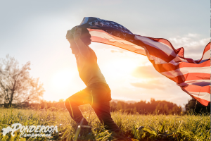 Person running through a field at sunset, waving an American flag