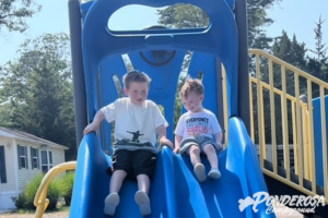 Two young boys are sitting on a slide at a playground sponsored by powdercom