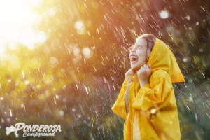 Person in a yellow raincoat smiling in the rain with bright sunlight behind them