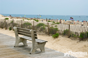A wooden bench is sitting on a wooden walkway next to a beach.