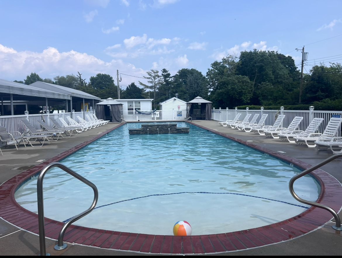 Outdoor swimming pool lined with white lounge chairs and a beach ball floating near the edge