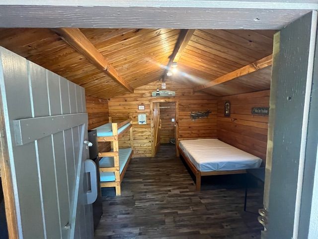 Rustic wooden cabin interior with bunk beds, a single bed, and a small table.