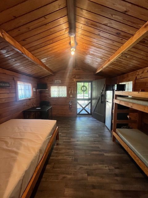Wood-paneled cabin bedroom with bunk beds, a single bed, and a door at the far end