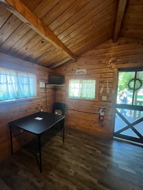 Wood-paneled cabin interior with a table, small windows, and a glass door with a round wreath.