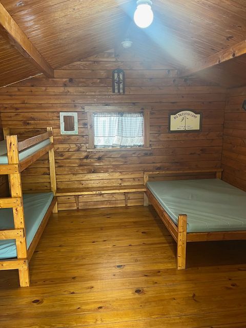 Wooden cabin bedroom with bunk bed, single bed, and a small window under a bright ceiling light.