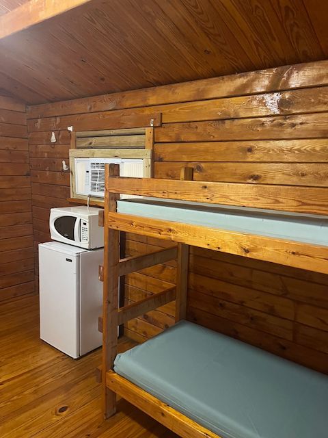 Small wooden loft room with bunk bed, mini fridge, microwave, and window air conditioner